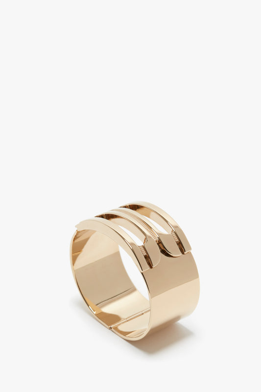 A gold-plated brass cuff bracelet with wide bands and a reflective surface, positioned upright against a plain white background, showcasing the elegant Exclusive Frame Bracelet In Gold design with a subtle Victoria Beckham logo.