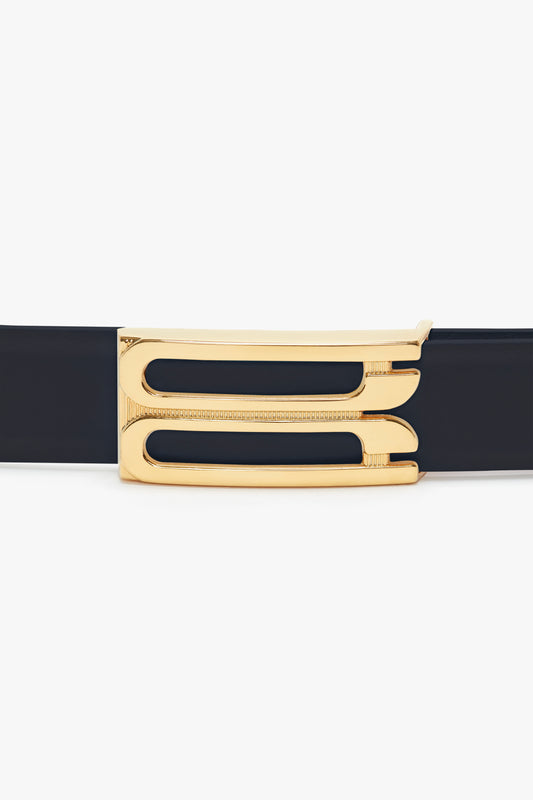 Elegant Exclusive Frame Belt in Midnight Navy Leather with a glossy gold buckle featuring a geometric cut-out design, isolated on a white background by Victoria Beckham.