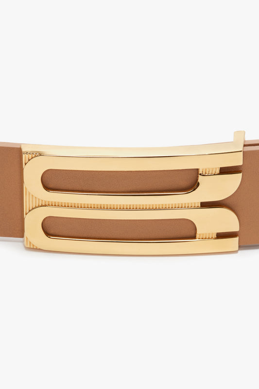 Close-up of a brown smooth calf leather belt with a unique, shiny gold Victoria Beckham hardware buckle featuring intricate linear details.
