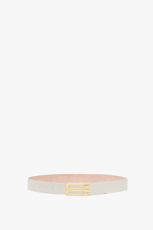 A contemporary Victoria Beckham Jumbo Frame Belt In Latte Leather crafted from thin, white calf leather with gold hardware displayed on a flat, light-colored surface against a plain white background.