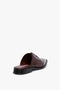 A single Victoria Beckham Flat Lace Up Mules In Bordeaux Leather with decorative perforations and a low heel, viewed from an angle showing both the back and side.