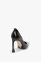 A single V Pump In Black Brushed Leather made of glossy material, featuring a sculptural heel and viewed from the back and slightly to the side, against a plain white background, by Victoria Beckham.