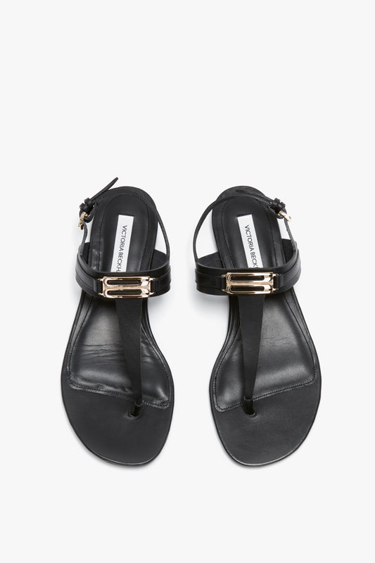 A pair of Flat Chain Sandal In Black Leather by Victoria Beckham with adjustable ankle straps, metallic buckle accents, and a chic SS24 design.