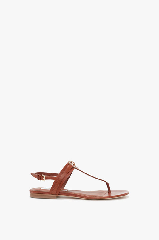 A single brown Flat Chain Sandal In Tan Leather by Victoria Beckham, with a minimalist design and an adjustable ankle strap, adorned with a subtle gold-tone chain, is displayed against a white background.