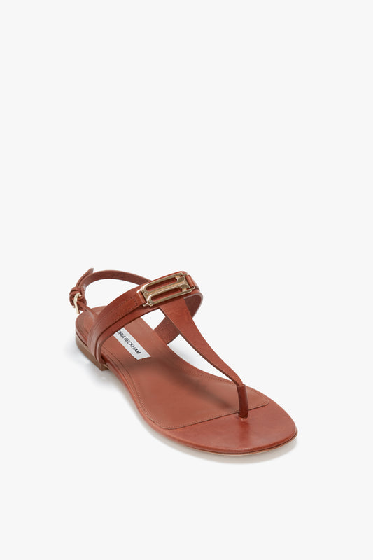 Victoria Beckham's Flat Chain Sandal in Tan Leather features a brown calfskin leather thong design with an adjustable ankle strap and gold buckle details.