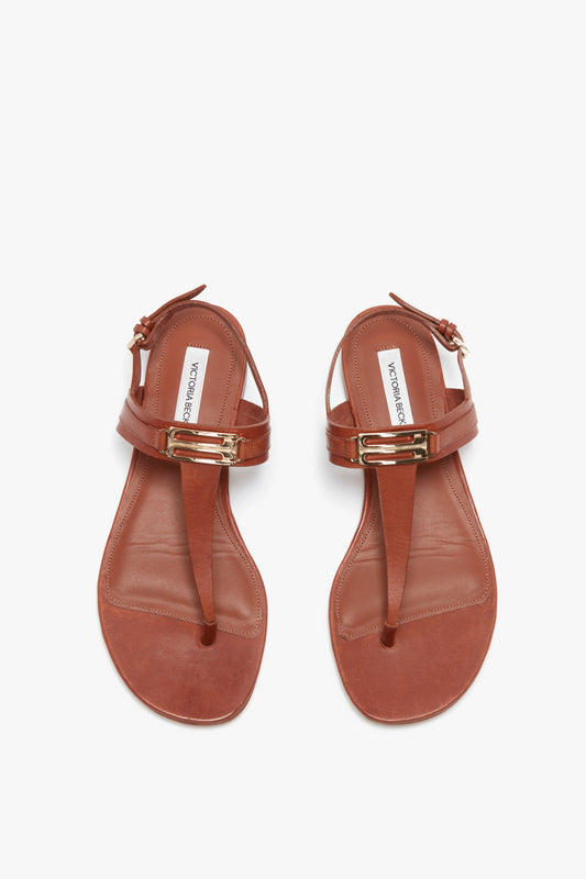 A pair of Victoria Beckham Flat Chain Sandal In Tan Leather featuring gold-tone hardware, an adjustable ankle strap, and a buckle fastening.