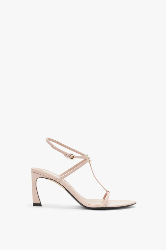 A Frame Detail Sandal In Nude Leather by Victoria Beckham with an open-toe design and a mid-height stiletto heel, featuring thin straps, an adjustable ankle strap, and a V-shaped sculptural heel.
