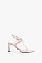 A Frame Detail Sandal In Nude Leather by Victoria Beckham with an open-toe design and a mid-height stiletto heel, featuring thin straps, an adjustable ankle strap, and a V-shaped sculptural heel.