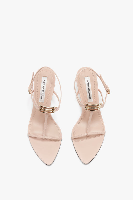 Top view of a pair of Victoria Beckham Frame Detail Sandal In Nude Leather featuring a single strap over the toes, adjustable ankle straps, and gold accents, all perched elegantly on V-shaped sculptural heels.