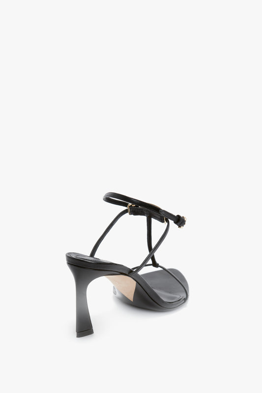 A black strappy high-heeled sandal, crafted from luxurious nappa leather, features a unique sculptural heel and an adjustable ankle strap. The **Victoria Beckham Frame Detail Sandal In Black Leather** is shown from the back on a white background.