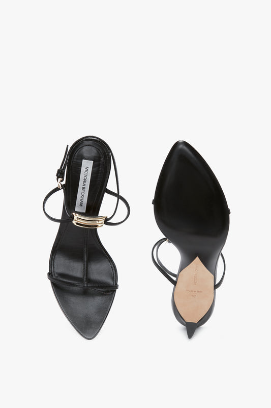 Pair of black Frame Detail Sandal In Black Leather by Victoria Beckham with sculptural heels, pointed toes, adjustable ankle straps, and a metallic accent on the top strap. One shoe is shown from above, and the other from the side on a white background.