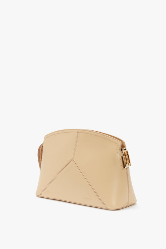 A glossy calf leather clutch bag with a geometric design and gold buckle detail, featuring a structured body, photographed against a plain white background. This versatile sesame-colored accessory elevates any outfit. Introducing the Victoria Clutch Bag In Sesame Leather by Victoria Beckham.