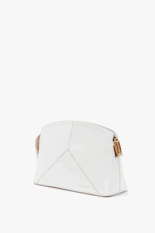 A white designer handbag with gold hardware, featuring geometric stitching and a sleek, structured design. Crafted from glossy calf leather, the Exclusive Victoria Clutch Bag In White Leather by Victoria Beckham boasts a subtly embossed brand name near the bottom.