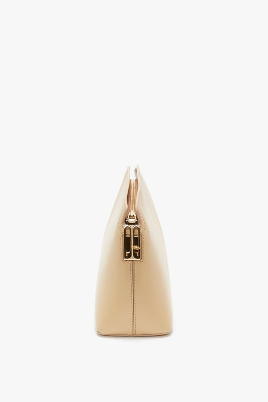 Side view of a beige, triangular-shaped handbag with a structured body and gold clasp closure on the top. This Victoria Beckham Victoria Clutch Bag In Sesame Leather exudes elegance and versatility.