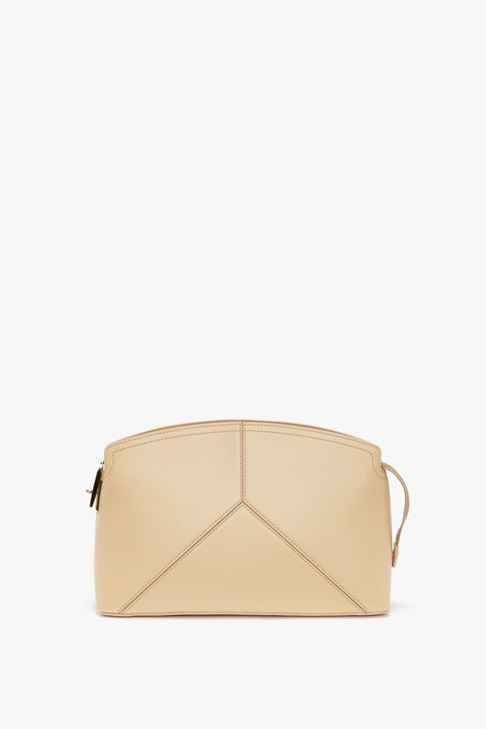 A Victoria Beckham Victoria Clutch Bag In Sesame Leather with a structured body and geometric design, featuring minimal stitching and a zip closure on the right side.