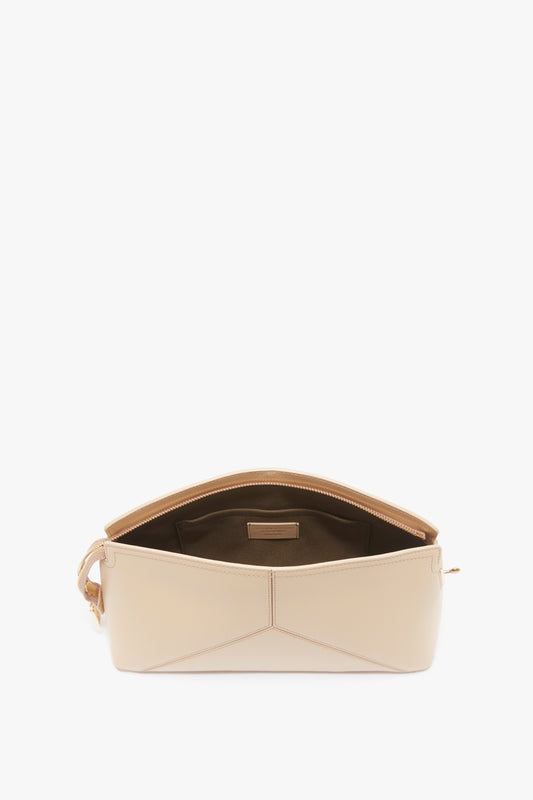 A versatile Victoria Beckham Victoria Clutch Bag In Sesame Leather with a zippered opening, revealing a structured body and brown interior with a small pocket.