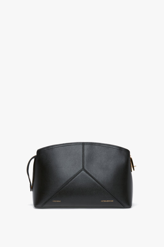 A Victoria Beckham Victoria Clutch Bag In Black Leather displayed against a white background. The bag features a minimalistic design with stitching details and a small gold logo at the bottom, showcasing a structured silhouette reminiscent of a Victoria Beckham leather clutch.