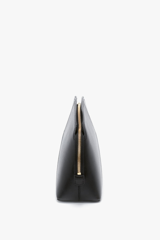 Side view of a Victoria Beckham Victoria Clutch Bag In Black Leather, with a structured silhouette and zippered closure, standing upright against a white background.
