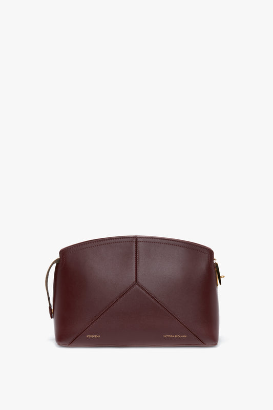 A Victoria Clutch Bag In Burgundy Leather with gold zippers and minimalist design, featuring the brand name "Victoria Beckham" at the bottom.