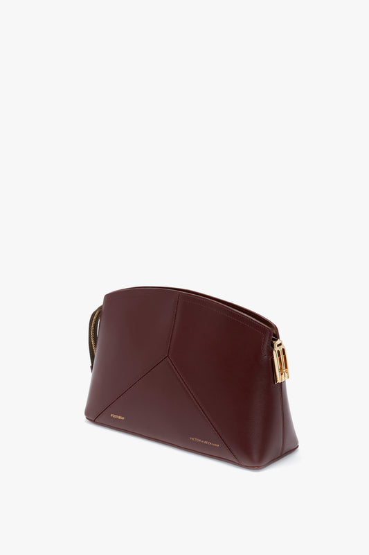 A **Victoria Clutch Bag In Burgundy Leather** from **Victoria Beckham**, with gold hardware and geometric stitching, reminiscent of Victoria Beckham’s elegant designs, is displayed on a white background.
