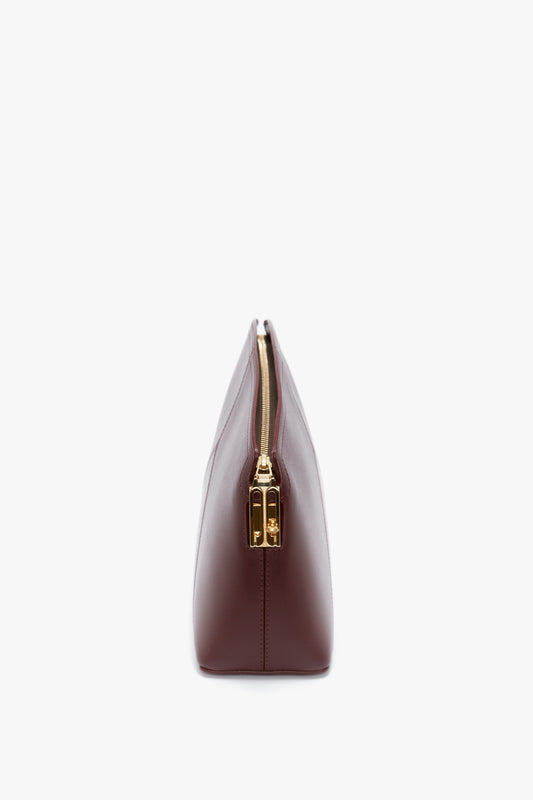 A side view of a closed, burgundy leather pouch with a gold zipper against a white background, reminiscent of the Victoria Beckham Victoria Clutch Bag In Burgundy Leather.
