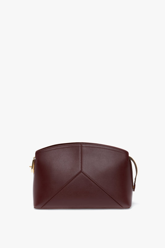 A Victoria Clutch Bag In Burgundy Leather with a geometric design on the front, featuring a zipper closure and a brown strap on the side, displayed against a white background. Perfect for those who appreciate Victoria Beckham's attention to detail.