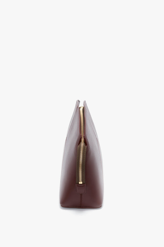Side view of a closed, rectangular, Victoria Beckham Victoria Clutch Bag In Burgundy Leather with a gold zipper on a white background.