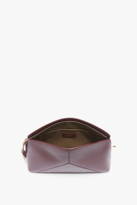 A burgundy leather handbag with a zipper partially open, revealing an empty interior; reminiscent of the sophisticated style of the Victoria Clutch Bag In Burgundy Leather by Victoria Beckham.