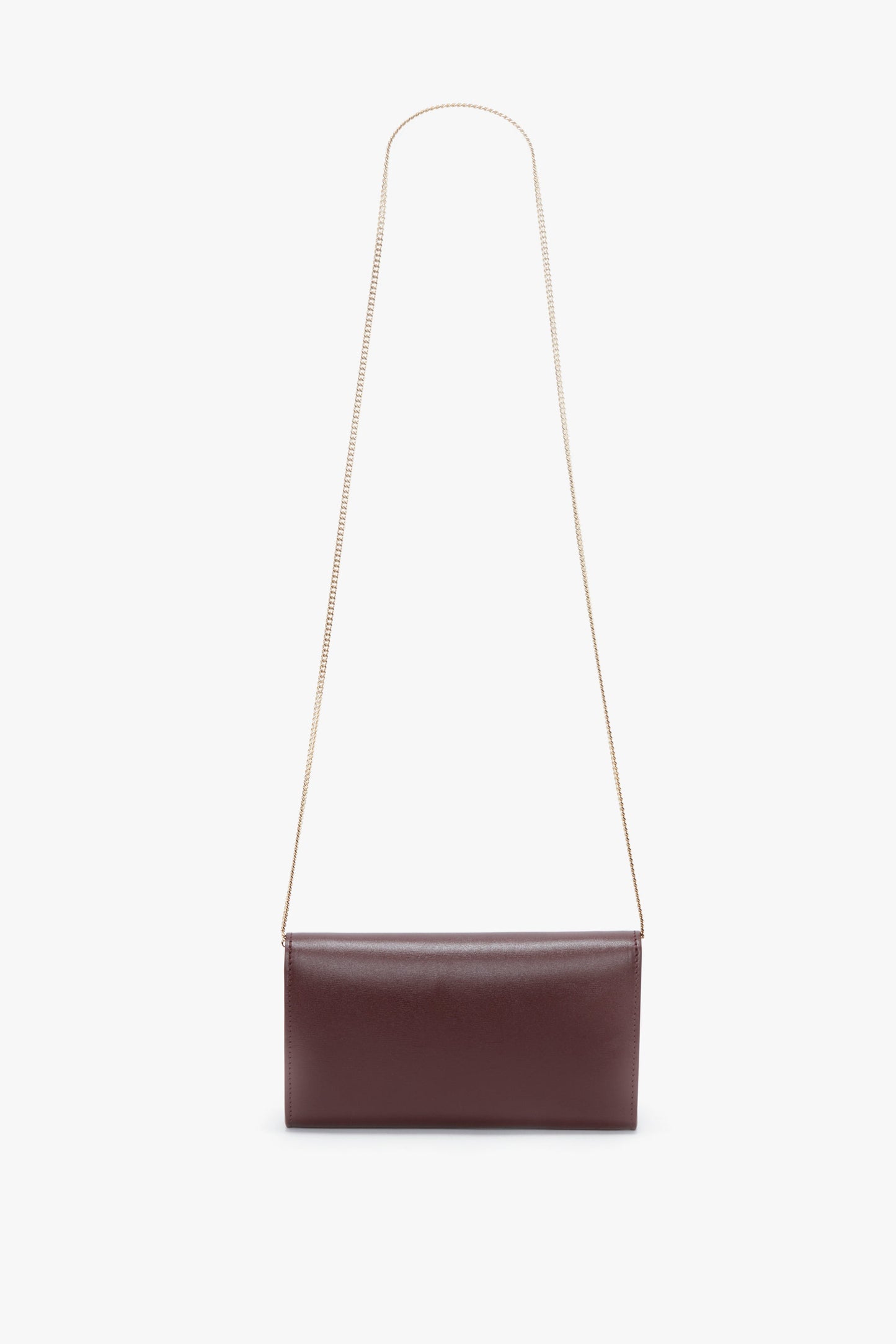 A rectangular, dark brown leather handbag with a long, thin gold chain strap, reminiscent of the Wallet On Chain In Burgundy Leather by Victoria Beckham, displayed against a white background.