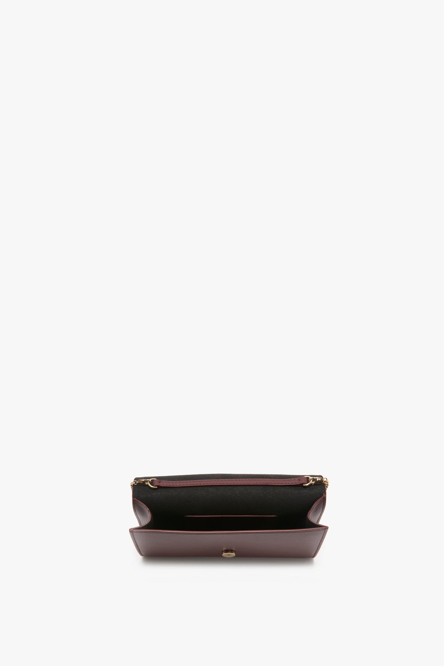 An open, empty Wallet On Chain In Burgundy Leather by Victoria Beckham with a snap button closure, complemented by a sophisticated black interior and a touch of elegance with its gold chain.