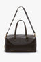 A Medium Gym Bag In Chocolate Brown by Victoria Beckham with dual handles and an adjustable shoulder strap, featuring gold-tone hardware and a structured design.