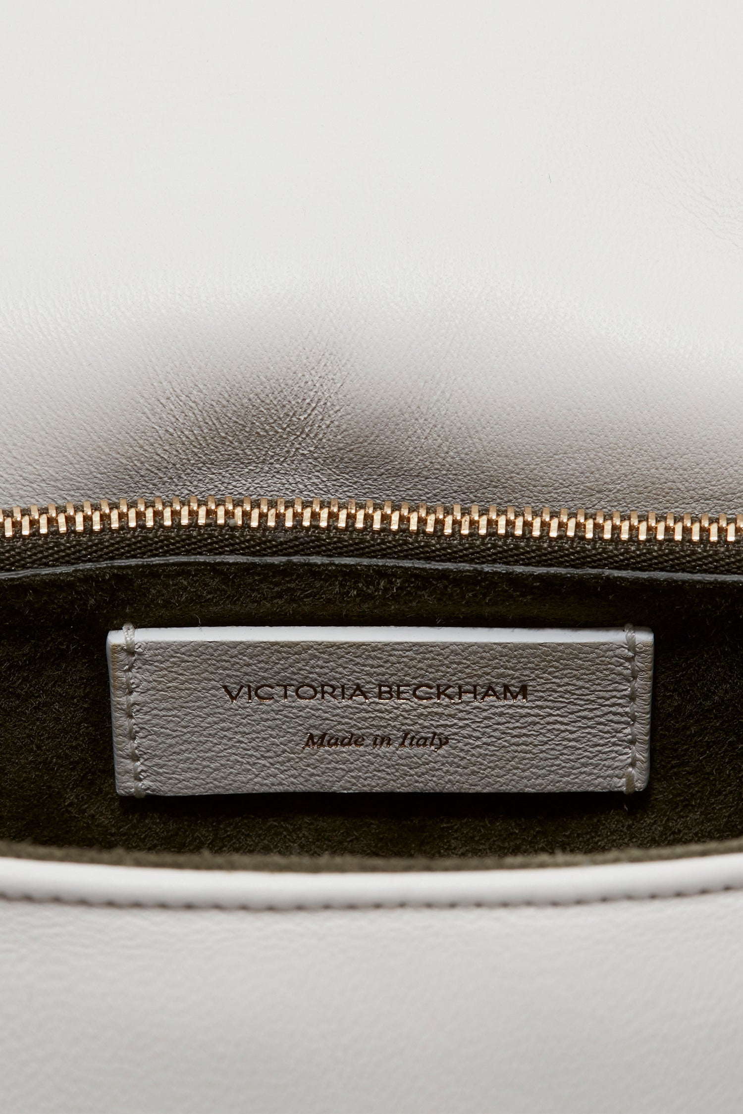 The interior label of a white leather Puffy Chain Pouch Bag With Strap In White Leather showing the text "Victoria Beckham Made in Italy" above the zipper, complemented by a detachable shoulder strap with gold chain detail.