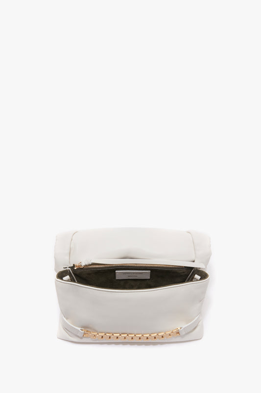 A Puffy Chain Pouch With Strap In White Leather from Victoria Beckham with an open top, revealing a zippered inner compartment lined with dark fabric. Gold studs adorn the outside, reminiscent of Victoria’s vintage watch straps.