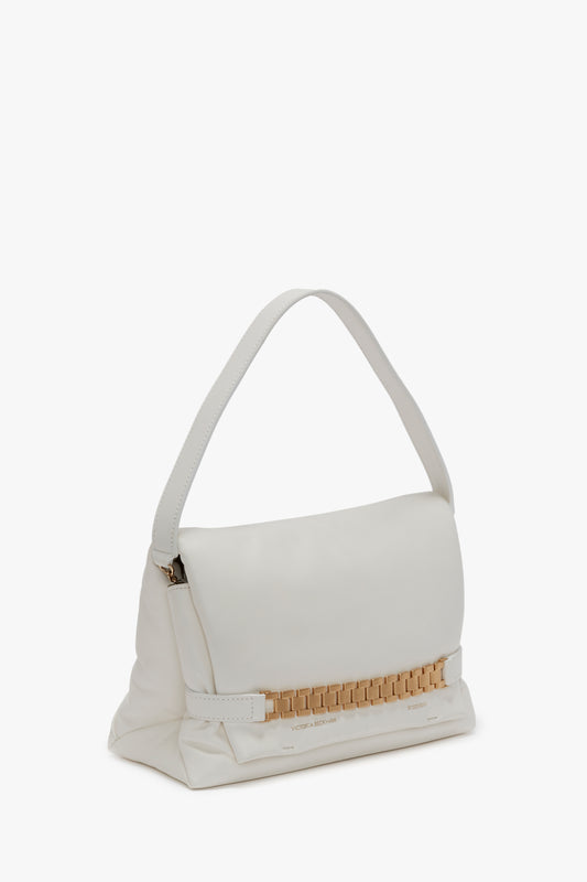 A Victoria Beckham Puffy Chain Pouch With Strap In White Leather with a short strap and gold detailing on the front, reminiscent of Victoria’s vintage watch straps, rests elegantly against a plain background.