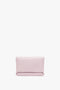 A Mini Chain Pouch Bag With Long Strap In Orchid Leather by Victoria Beckham, with a minimalist design, reminiscent of an orchid's delicate hue, sits elegantly against a white background.