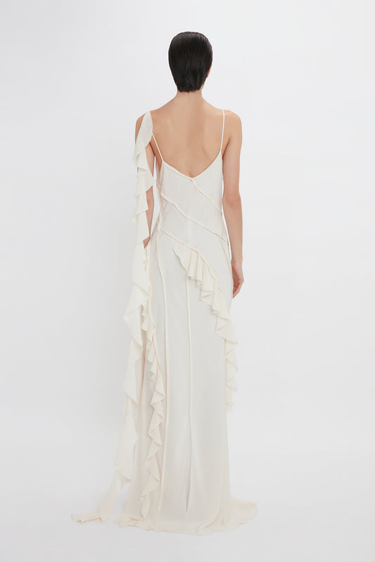 Woman in an elegant Victoria Beckham Exclusive Asymmetric Bias Frill Dress In Ivory with ruffled detailing, viewed from behind against a plain background.