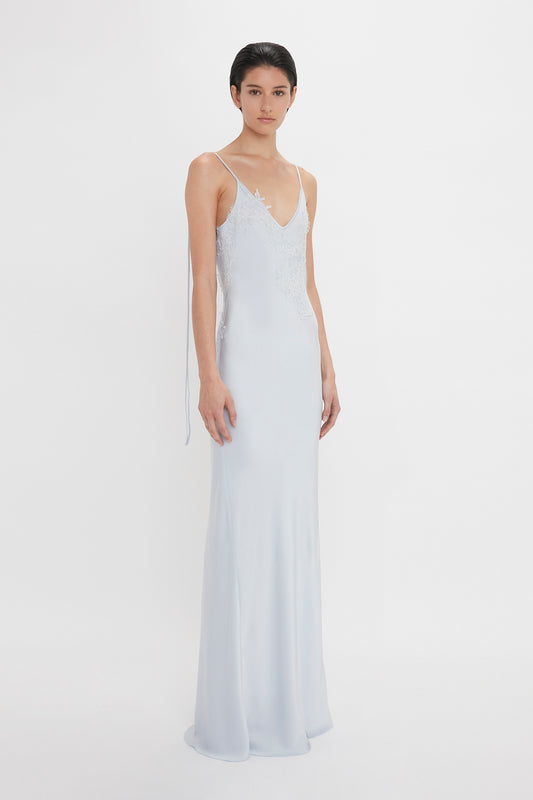 Woman in a light blue crepe back satin dress with lace detailing, standing against a white background. (Exclusive Lace Detail Floor-Length Cami Dress In Ice by Victoria Beckham)