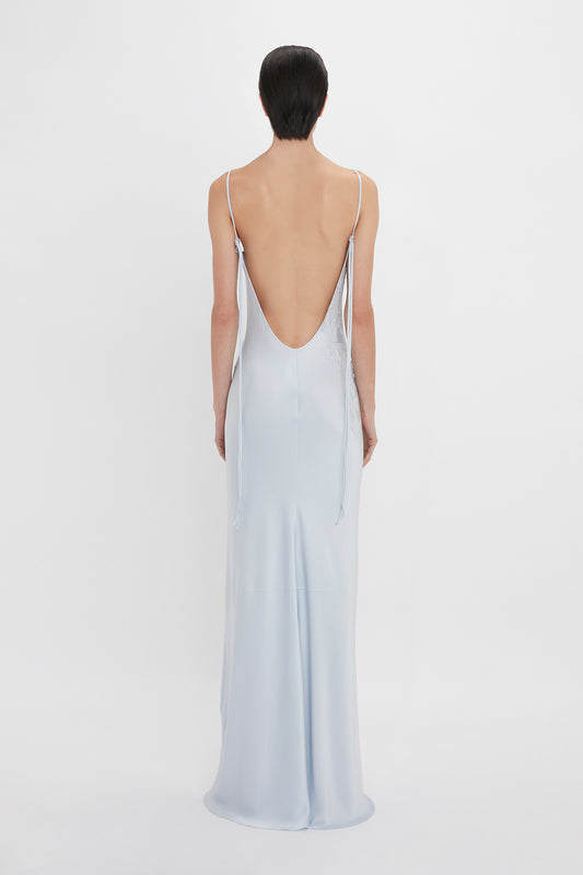 A woman with short dark hair is shown from the back, wearing a Victoria Beckham Exclusive Lace Detail Floor-Length Cami Dress In Ice with thin straps and lace detail.