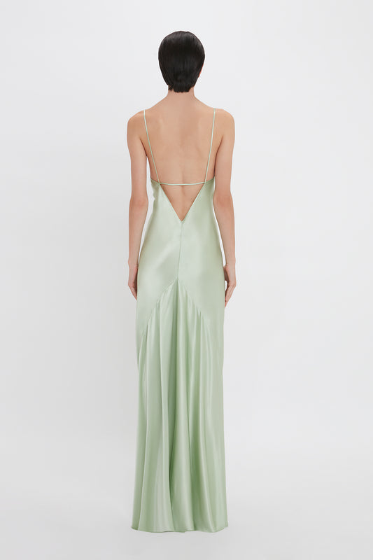 A woman stands with her back to the camera, wearing a Victoria Beckham Exclusive Low Back Cami Floor-Length Dress In Jade with a low-cut back and thin straps.