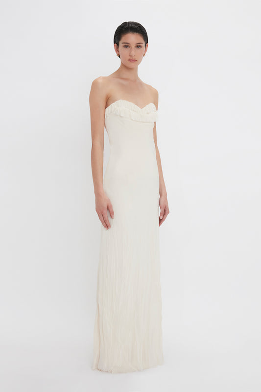 A woman in a Victoria Beckham Exclusive Floor-Length Corset Detail Gown in Ivory standing against a white background.