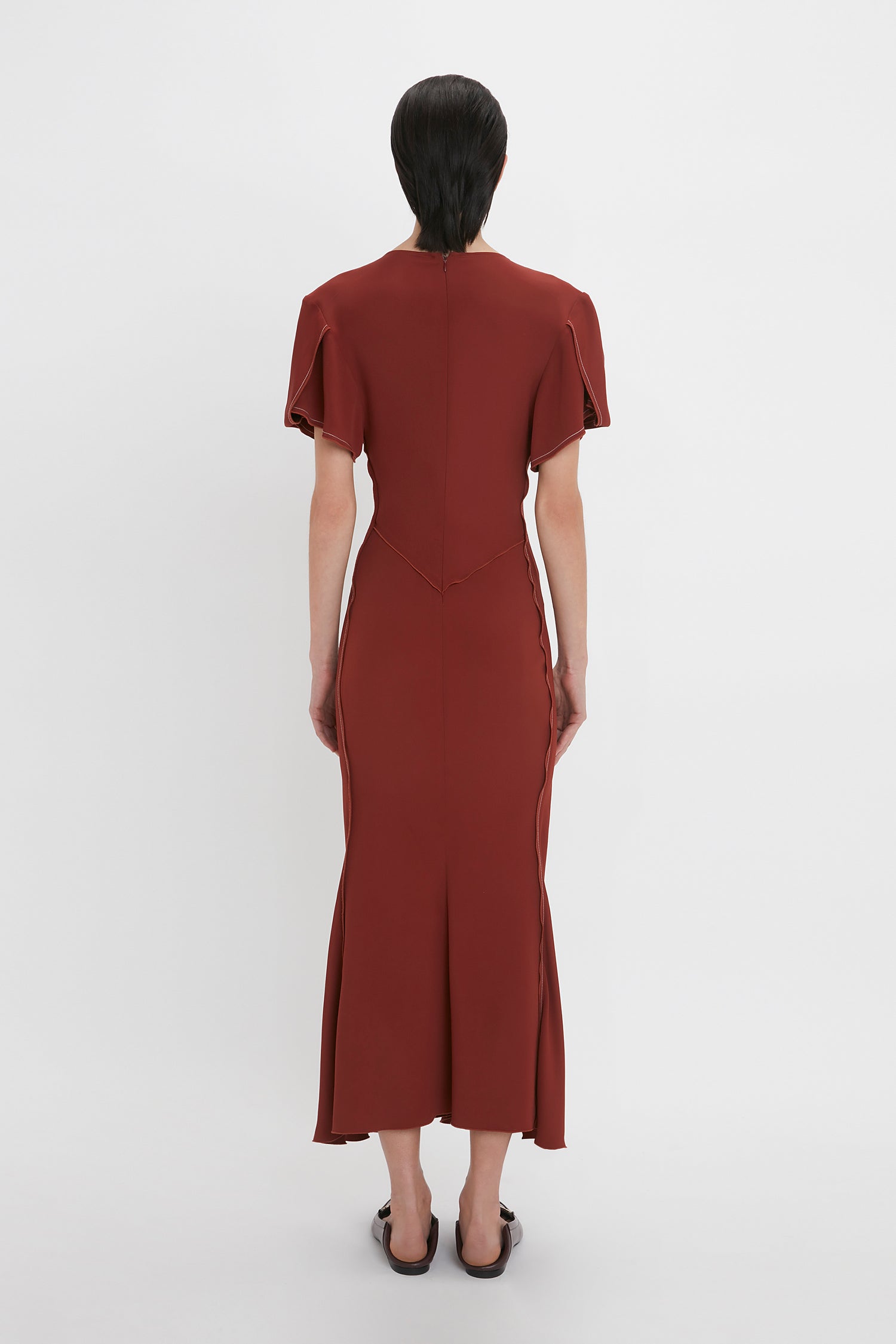Person with short, dark hair wearing the Gathered V-Neck Midi Dress In Russet by Victoria Beckham, photographed from the back against a plain white background.