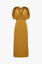 A Victoria Beckham V-Neck Ruffle Midi Dress In Harvest Gold with short puffed sleeves, a deep v-neck, and gathered detailing at the shoulder and waist exudes a seductive quality.