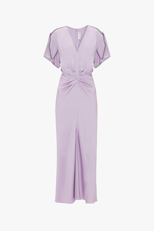Sure, here is the revised sentence:

A lavender-colored, short-sleeve midi dress with a V-neck and waist-defining pleat detail. The Gathered V-Neck Midi Dress In Petunia by Victoria Beckham features an ankle-length front slit and dark piping accents on the sleeves.