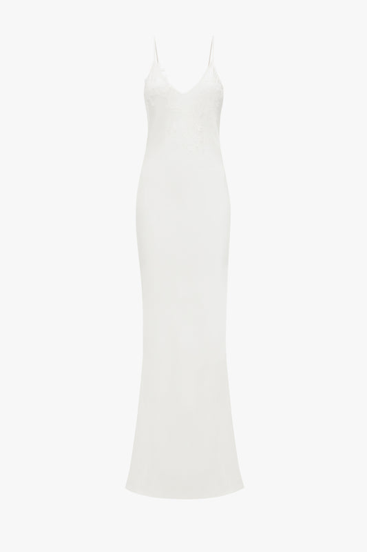 A white, sleeveless, floor-length evening dress with lace appliqué on the bodice, displayed against a white background by Victoria Beckham's Exclusive Lace Detail Floor-Length Cami Dress In Ivory.