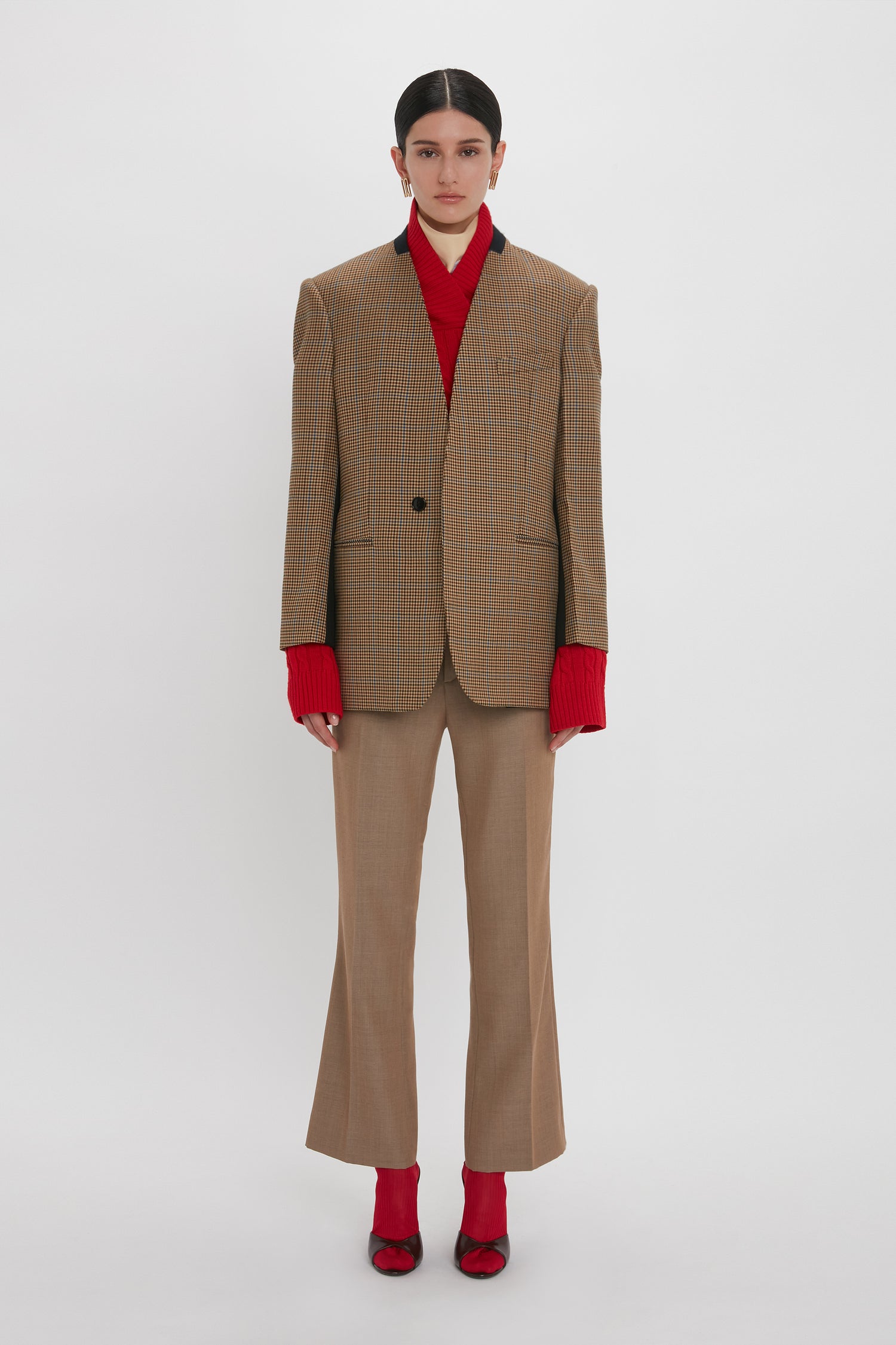 A person stands against a plain background wearing the Victoria Beckham Pocket Detail Collarless Jacket In Tobacco with a modern oversized fit, matching pants, a red turtleneck sweater, and red shoes.