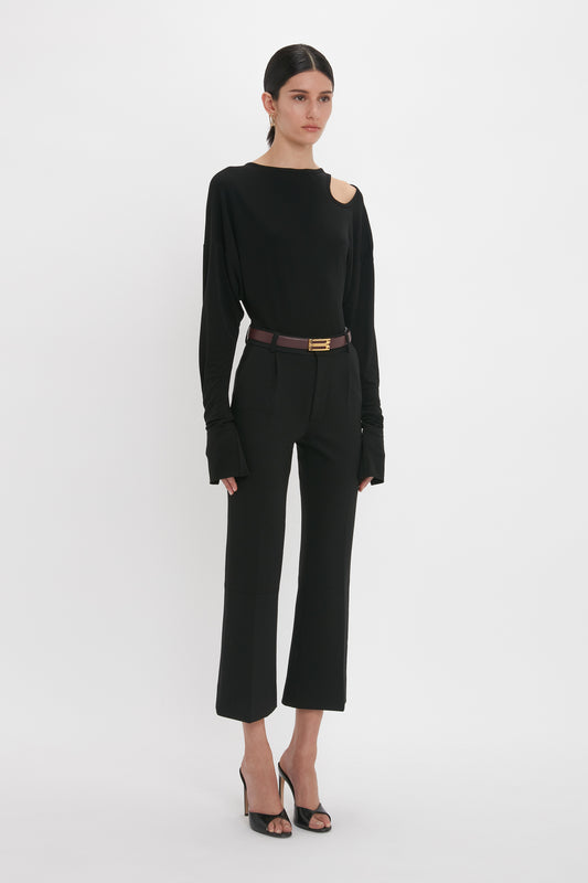 A woman in a Victoria Beckham Twist Detail Jersey Top In Black and trousers, accessorized with a belt, poses against a white background.