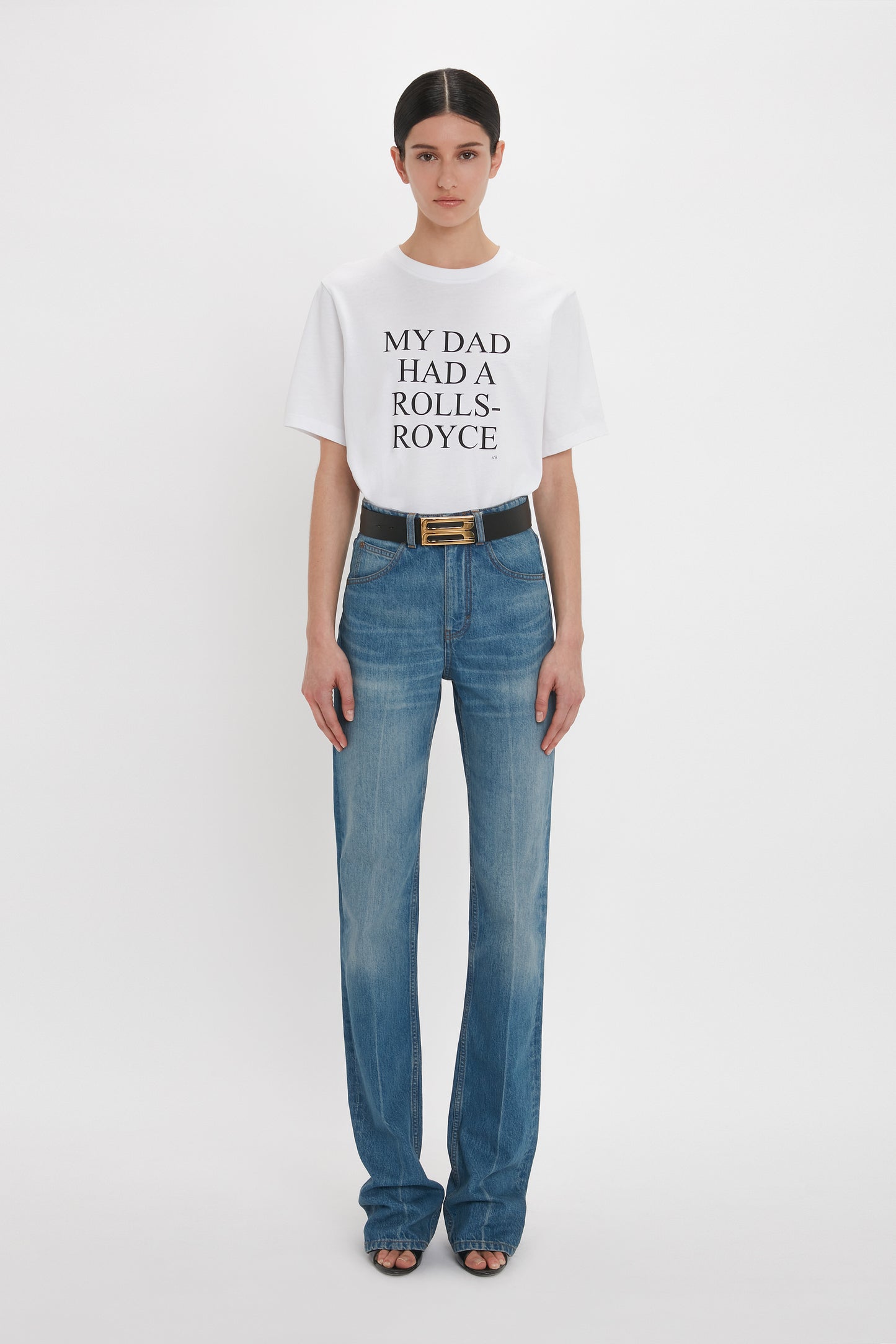 A person stands against a white background wearing a white T-shirt with the text "MY DAD HAD A ROLLS-ROYCE" and blue jeans crafted from distressed Broken Vintage Wash 100% cotton denim, specifically the Julia Jean In Broken Vintage Wash by Victoria Beckham.