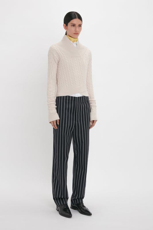Person wearing a beige knitted sweater and Victoria Beckham Tapered Leg Trouser In Midnight-White, standing against a plain white background.