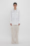 A person stands against a white background wearing an Oversized Pocket Shirt In White by Victoria Beckham made of organic cotton and light beige Relaxed Cargo Trouser.