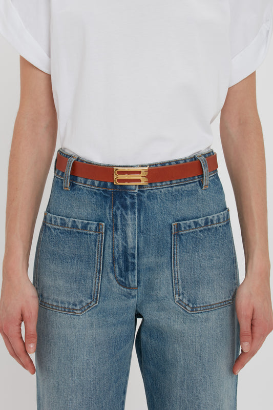 Close-up of a person wearing jeans and a white t-shirt, accented with a Victoria Beckham calf leather belt featuring gold hardware.